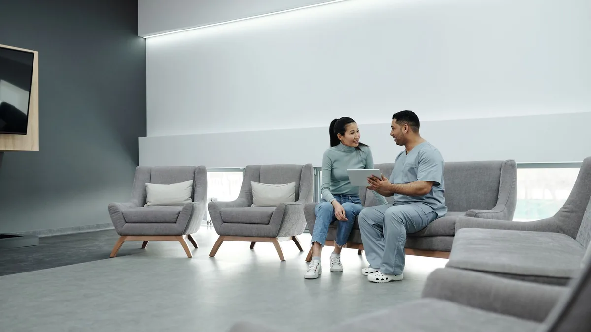 Doctor and patient discussing health in a modern waiting room with digital tablet.