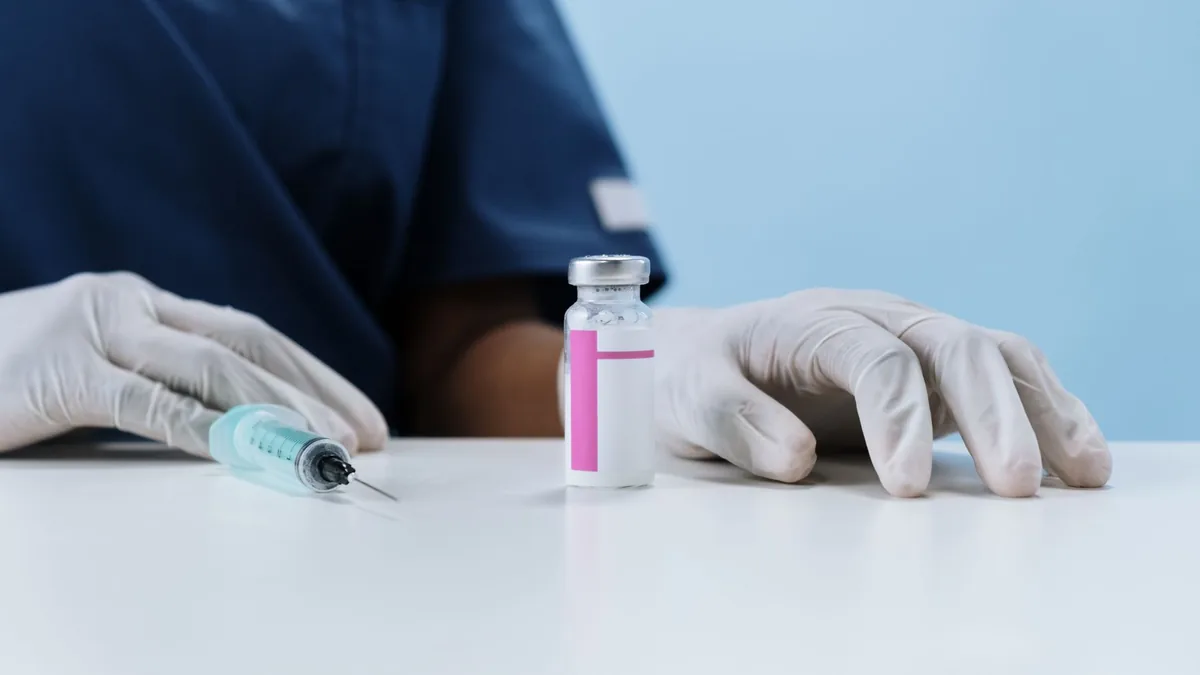 Close-up of healthcare worker's gloved hands with syringe and vaccine vial on a table.