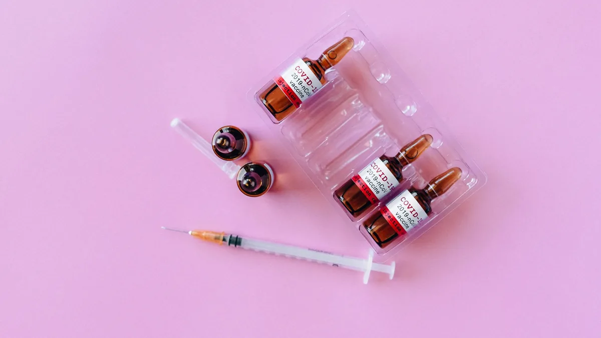 Top view of COVID-19 vaccine vials with syringe on a pink background.