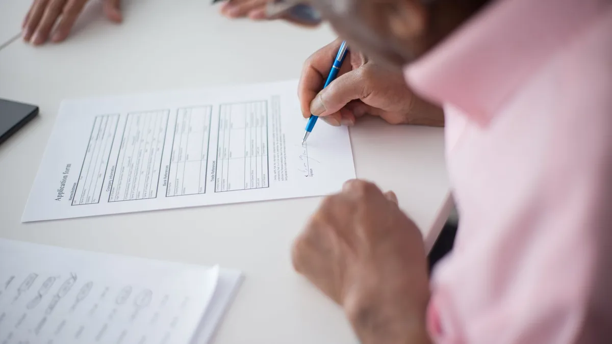 Elderly man signing important business document at desk in office setting.